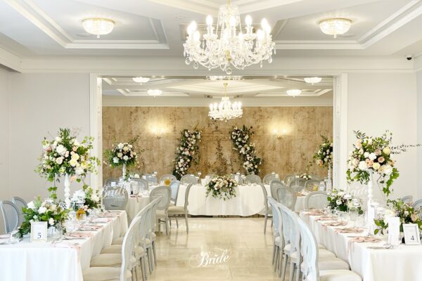 Piękna dekoracja weselna beżowymi obrusami i dużą ilością kwiatów na białych stojakach