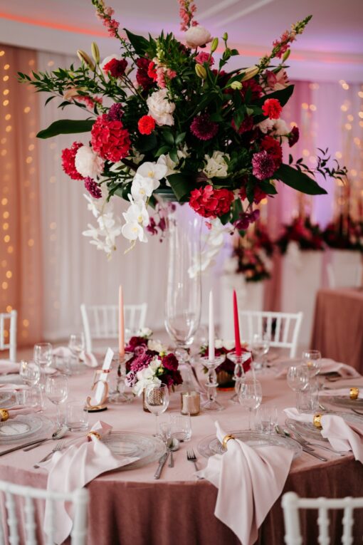 Ogromne kompozycje kwiatowe na szklanych wazonach wśród różowych stołów.