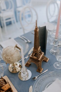 Dekoracja wesela w stylu podróżniczym na niebieskim obrusie ze złota wieża Eiffla i globusem