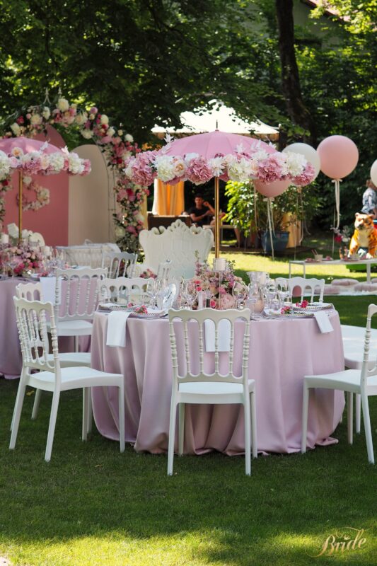 Ogród udekorowany różowymi stołami z parasolami z kwiatów i różowe balony na helu.