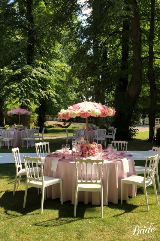 Dekoracja stołu na chrzciny z różowymi obrusami i dekoracją z parasoli pokrytymi kwiatami.