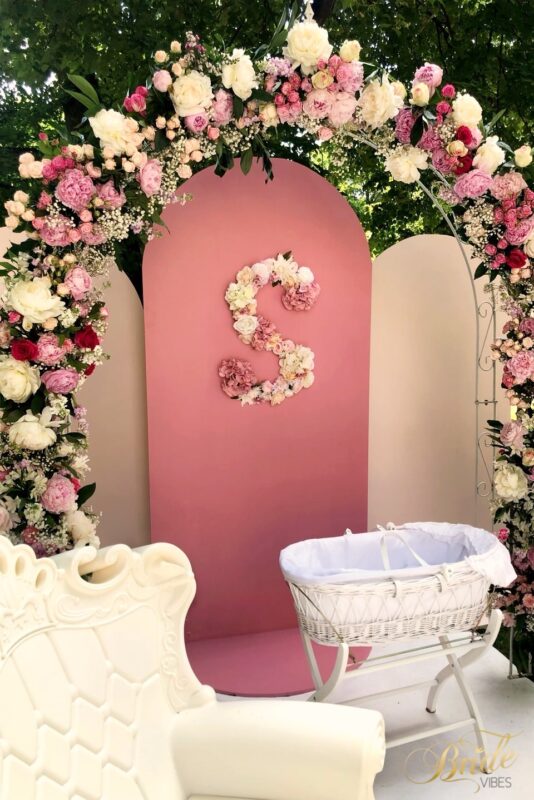 Różowa ścianka do zdjęć z różowo białą girlandą kwiatową.