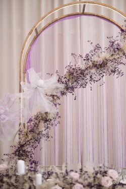 Złote łuki ubrane w fioletowe makarony z girlandą kwiatową.